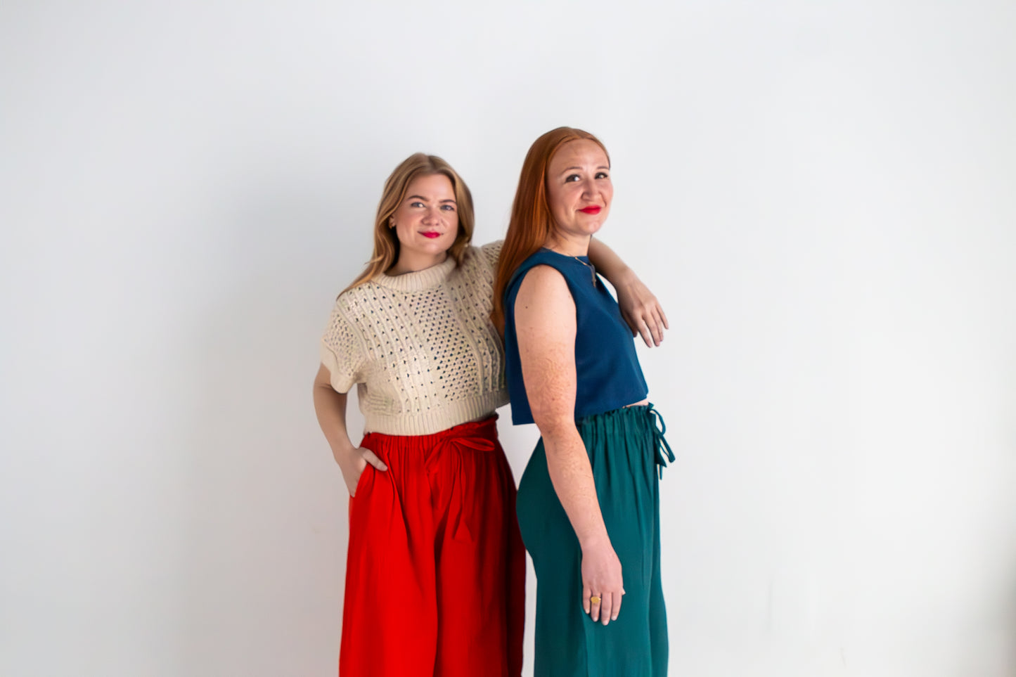 Two women standing back-to-back against a white background, wearing colorful outfits.