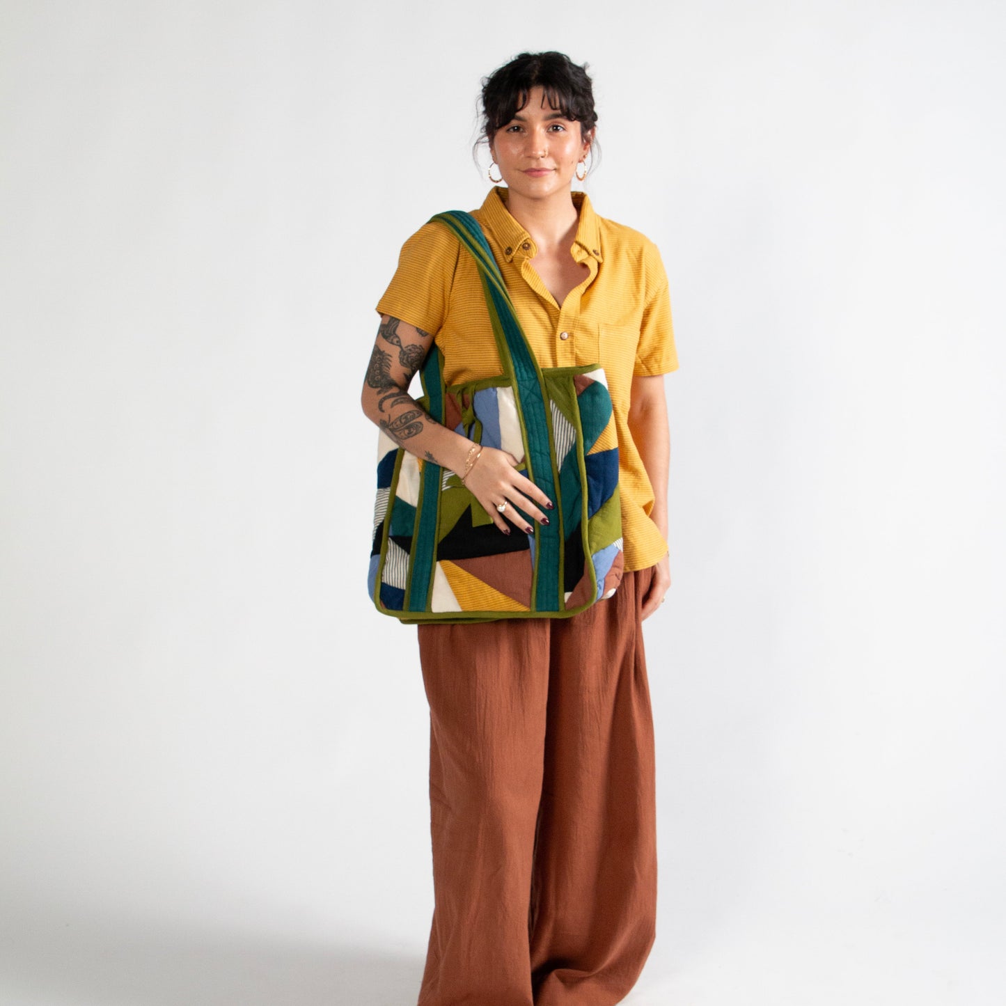 Person wearing a yellow shirt and brown pants with a colorful bag on a white background