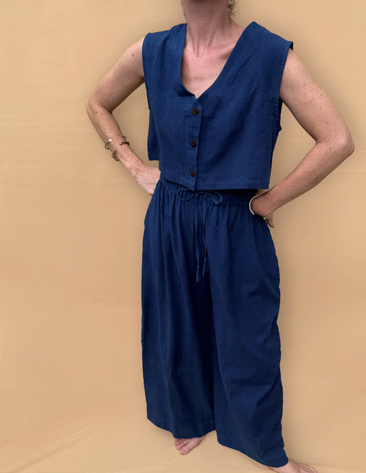 Person wearing a blue sleeveless top and wide-leg pants against a beige background