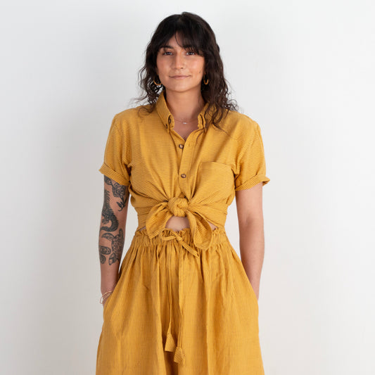 Woman wearing a mustard yellow top and skirt against a white background