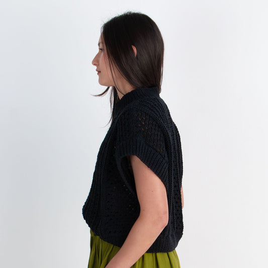 Woman wearing a black top and green skirt standing against a white background
