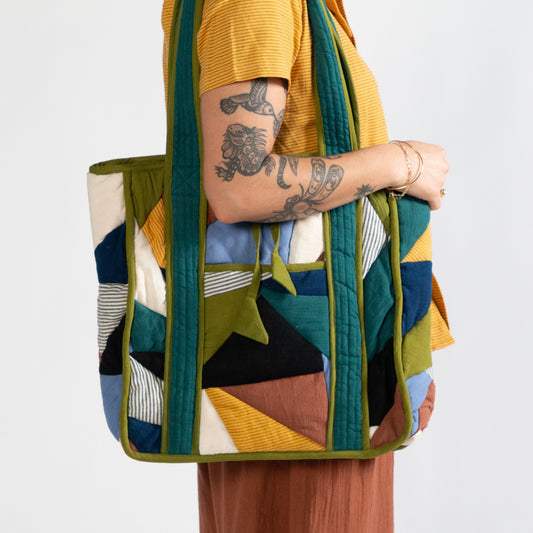 Person holding a colorful quilted bag against a white background