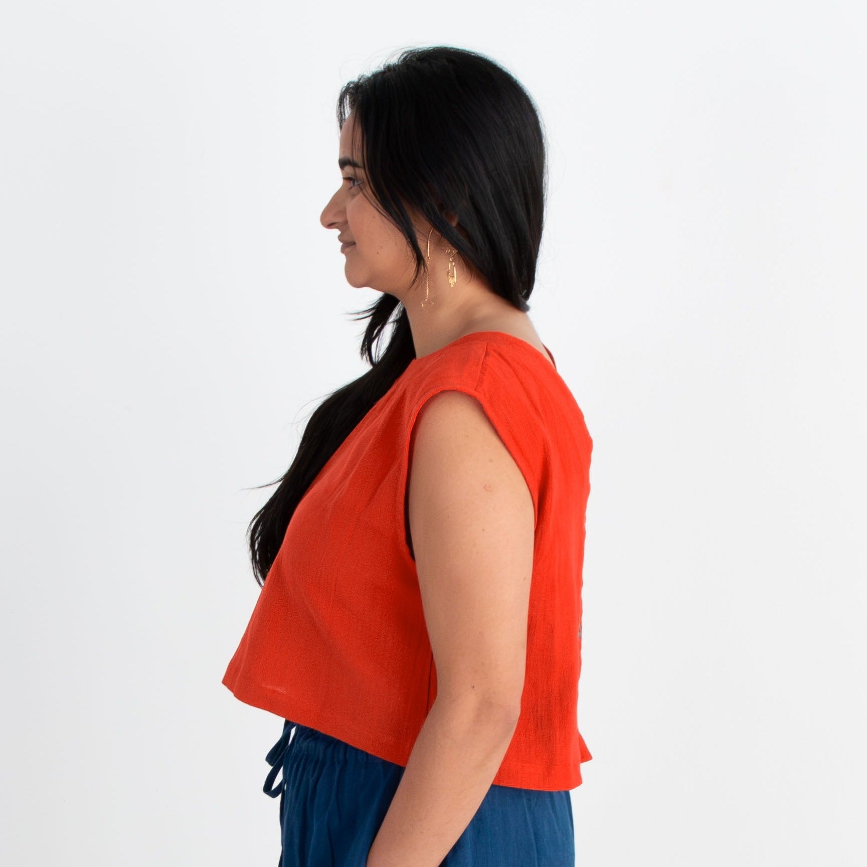 Woman wearing a red top and blue pants standing against a white background