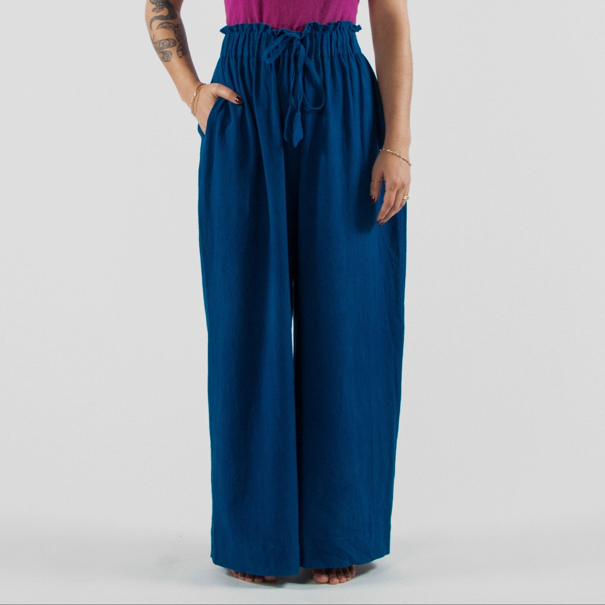 Woman wearing a purple top and blue pants standing on a white studio backdrop.