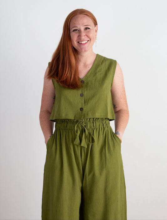 Woman wearing a green sleeveless top and pants against a white background