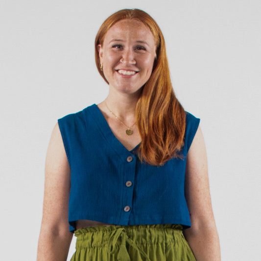 Woman wearing a blue sleeveless top and green wide-leg pants standing in front of a white backdrop with photography equipment.