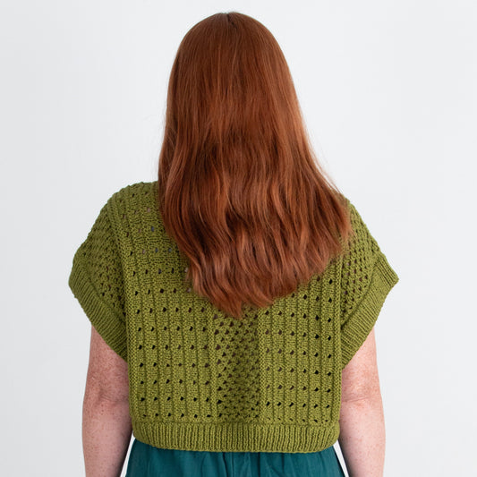 Person wearing a green knitted top and teal pants on a plain background