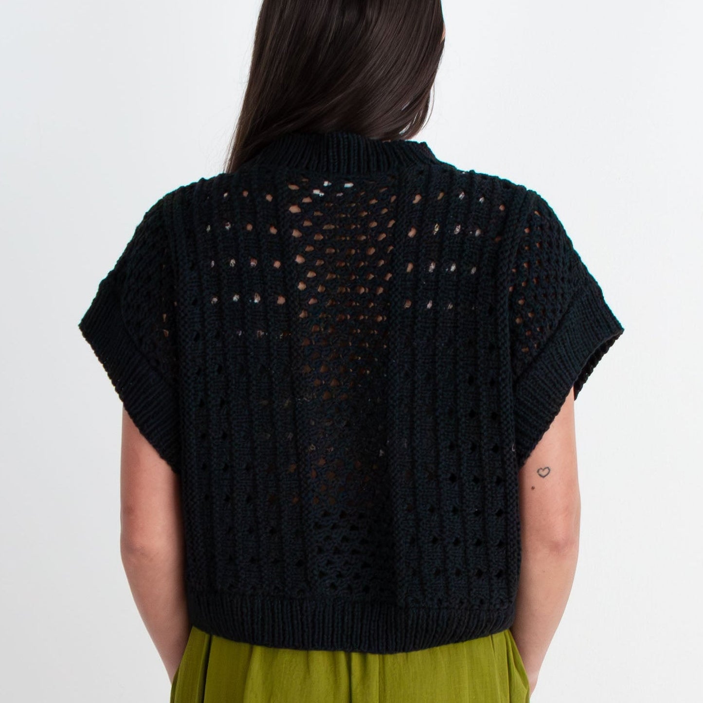 Person wearing a black top and green skirt standing on a white background