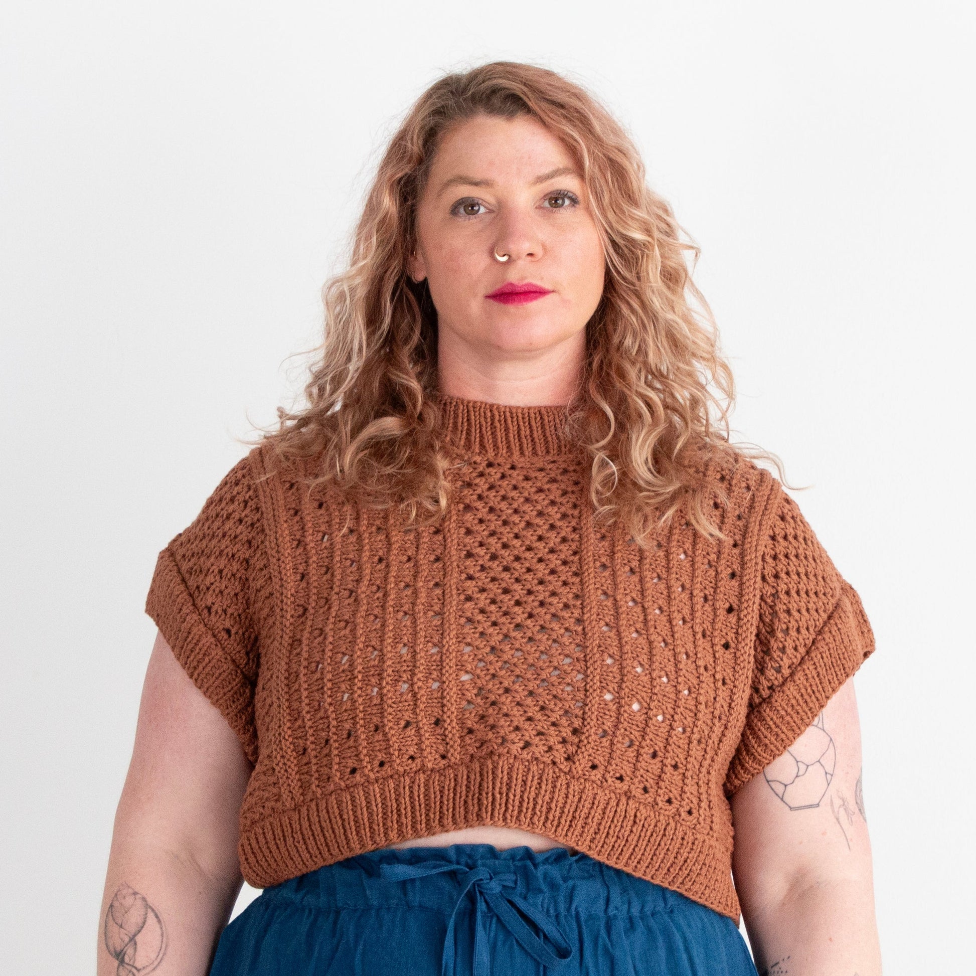 Woman wearing a brown knitted top and blue pants on a white background