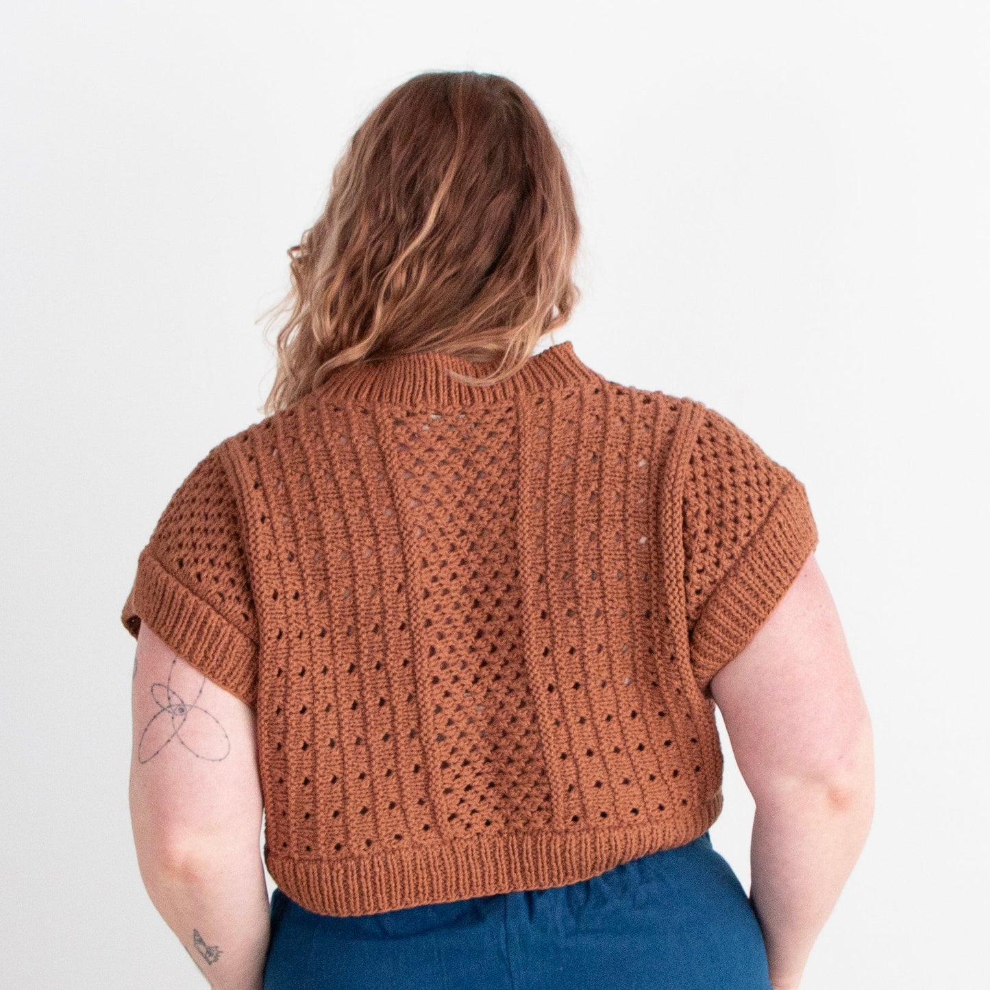 Person wearing a brown knitted sweater and blue pants on a white background